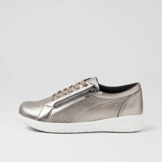 A metallic silver slip-on sneaker with a textured leather-like finish, matching silver laces, a zippered side detail, and a thick white sole, shown against a light gray background.